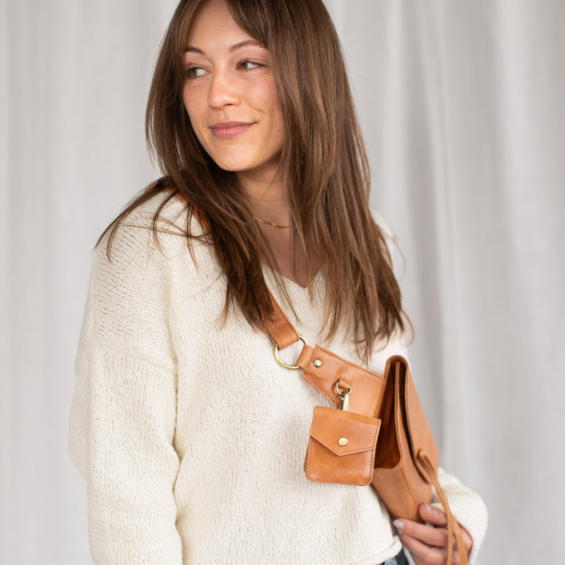 Woman wearing white sweater and crossbody with Airpod case attached